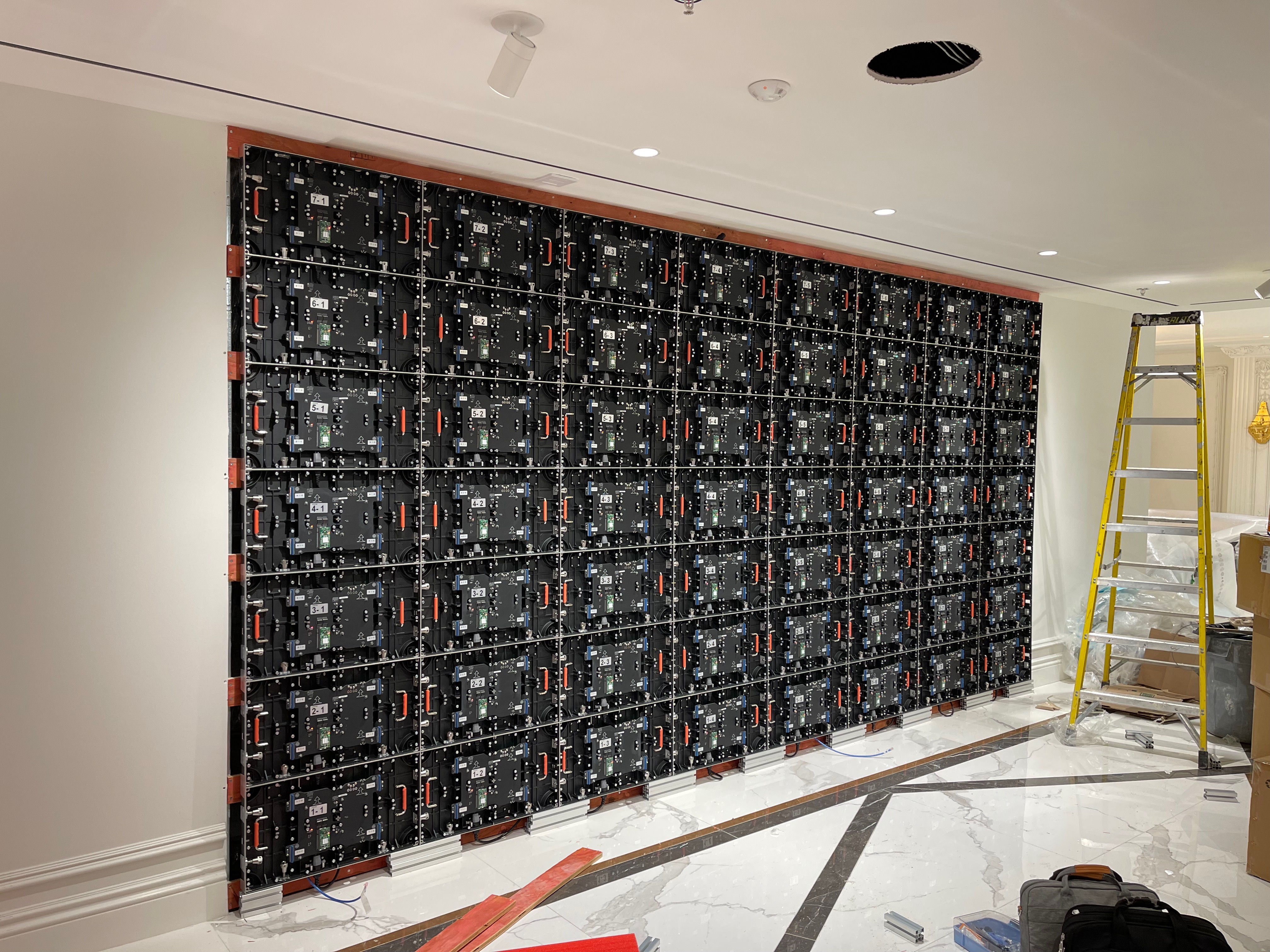 Rear of a fine pitch LED wall under installation — numbered cabinets on an aluminium rail and timber sub-frame with power and data looms