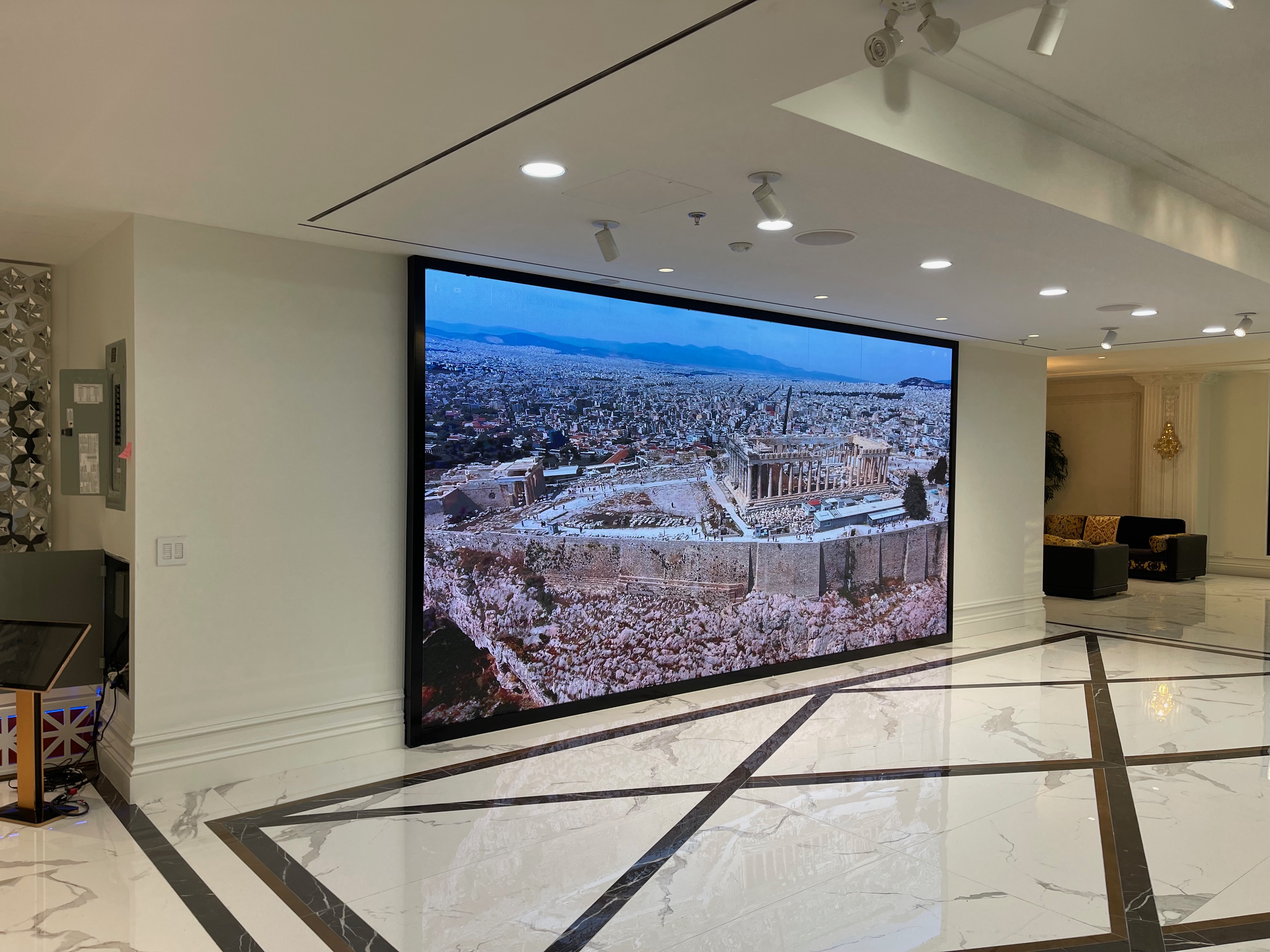 Fine pitch LED video wall installed flush into a marble commercial lobby wall, playing an aerial cityscape at full brightness under ceiling downlights