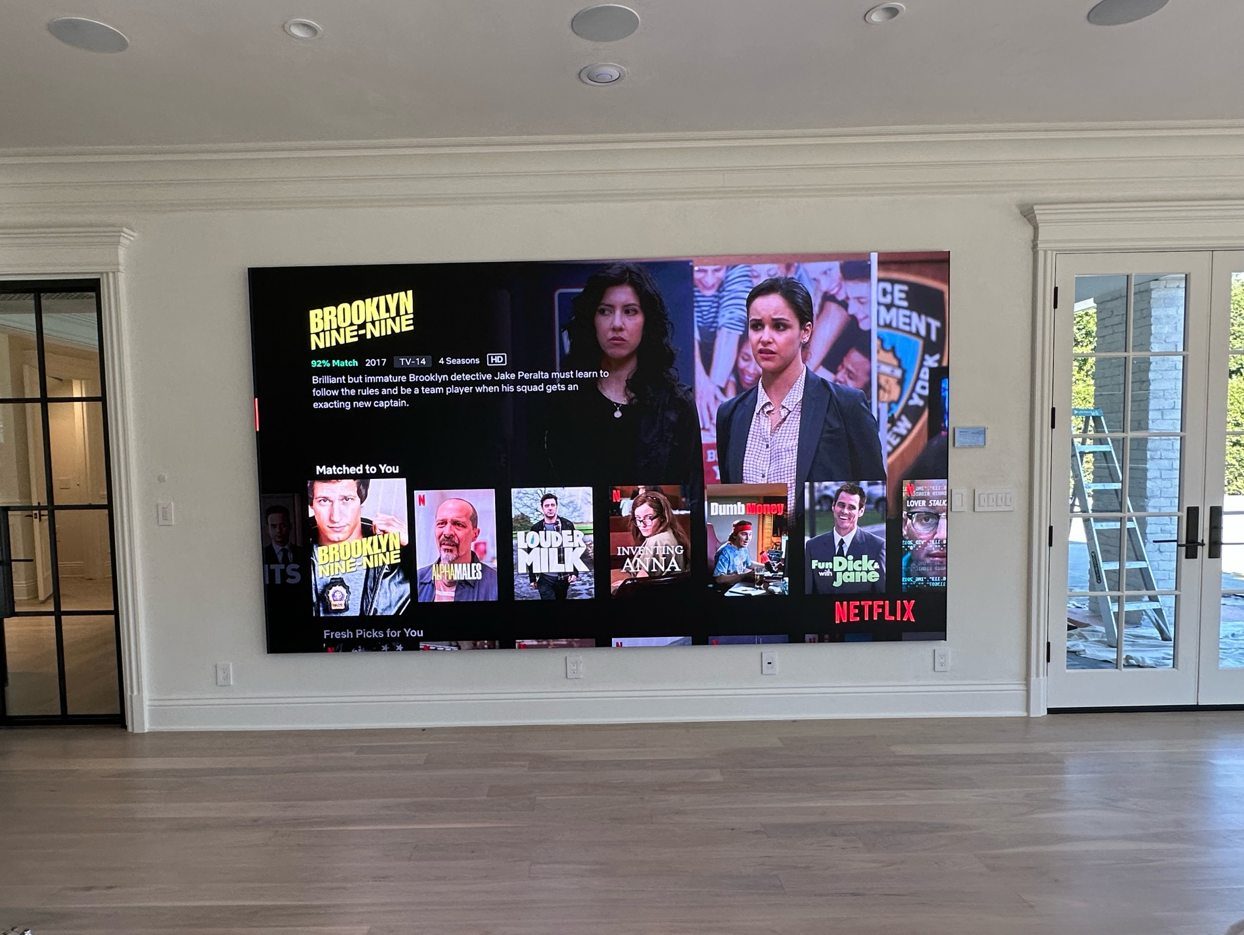 Large fine pitch COB LED screen mounted flush on a living room wall showing a streaming interface in a bright room with daylight from french doors