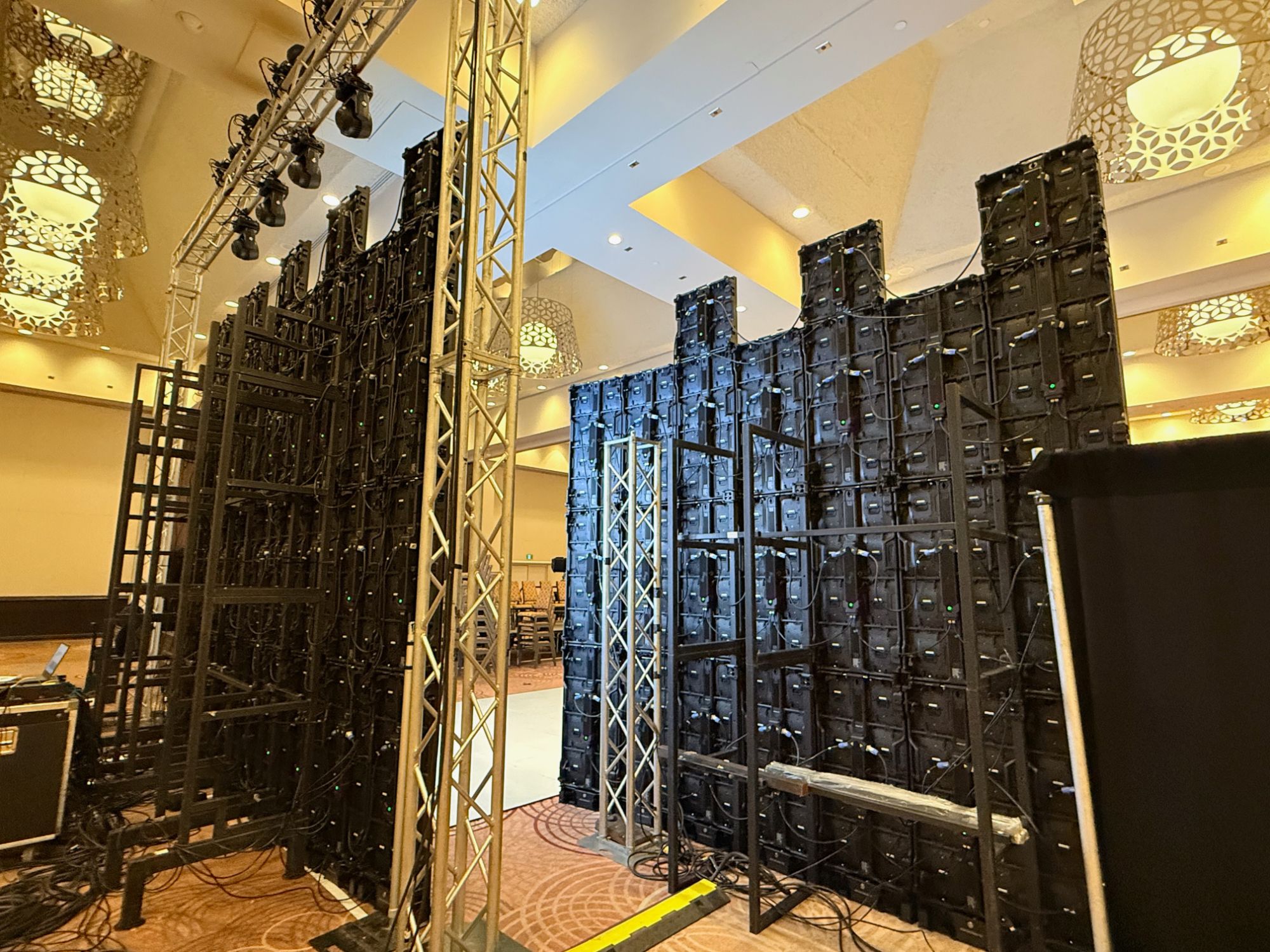 P2.6mm panels stacked on ground-support frames in a hotel ballroom, rear view showing the frame, base plates and power runs