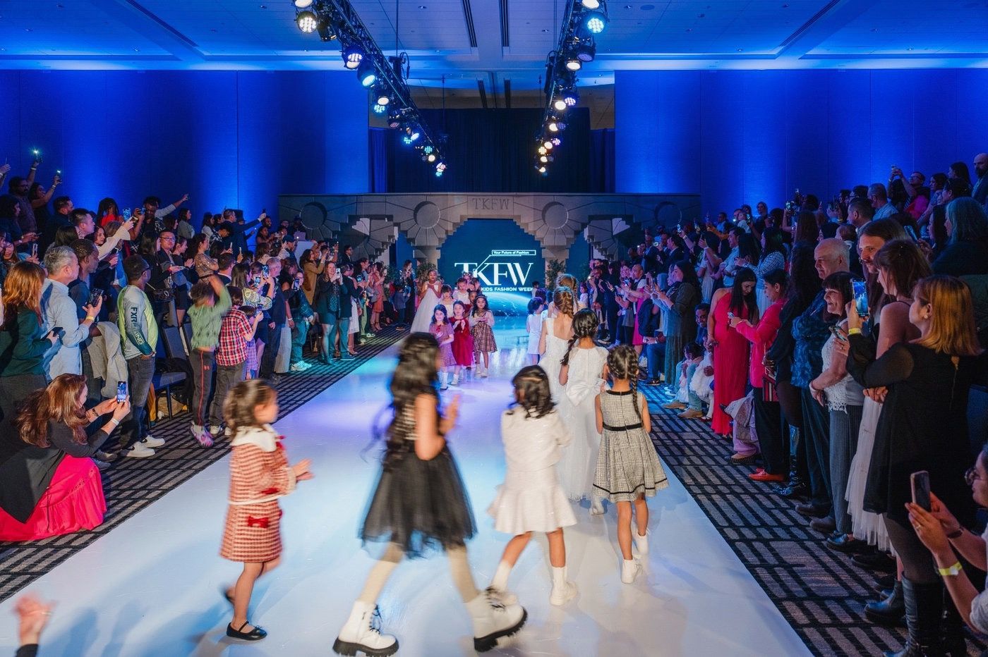 TKFW finale walk — full house standing both sides of a white runway with the TKFW LED backdrop