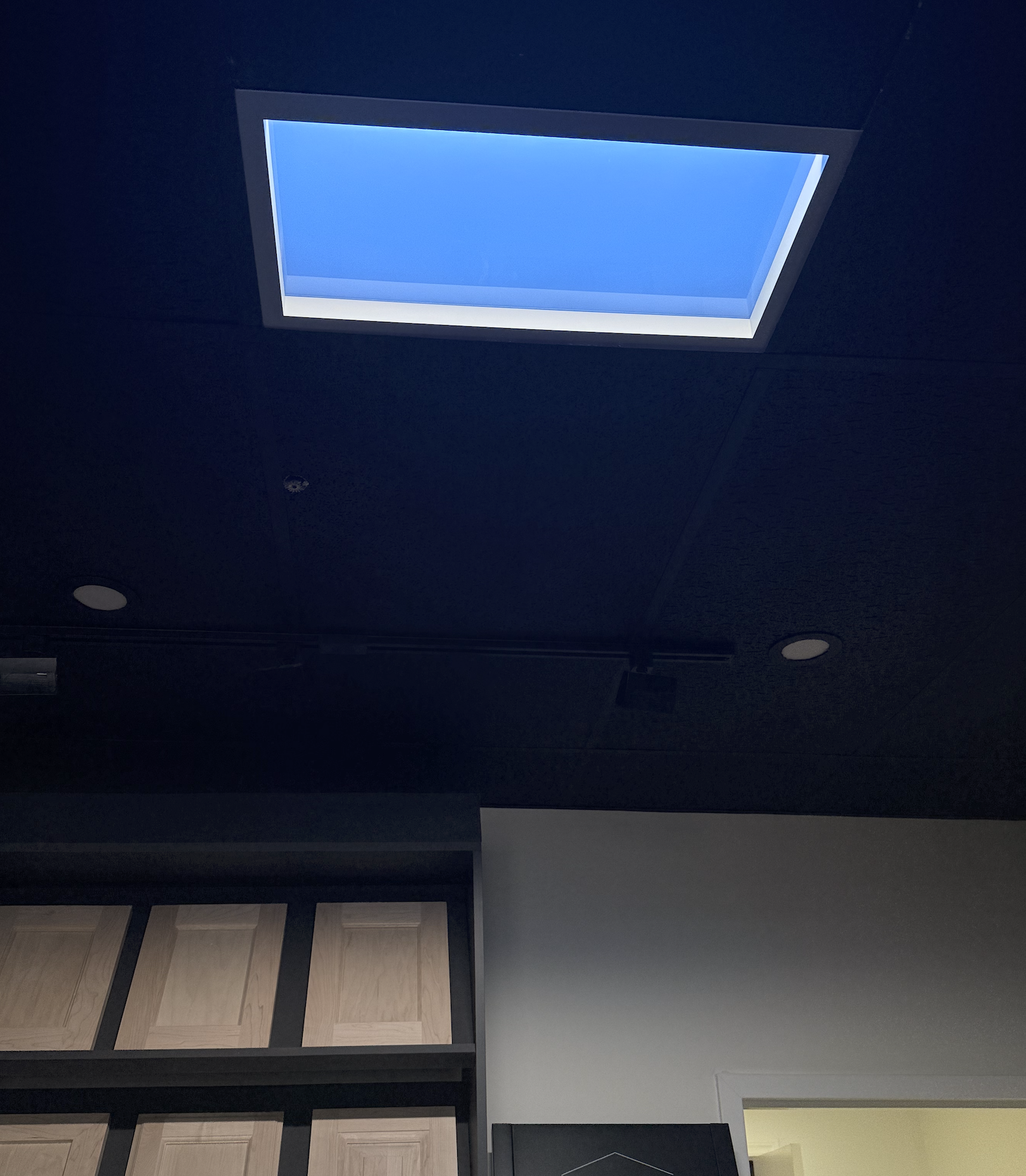 LED skylight panel glowing bright blue in a black showroom ceiling above cabinet-door samples